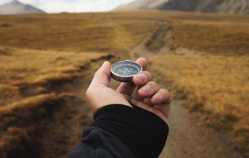 Hand holding compass walking mountain path