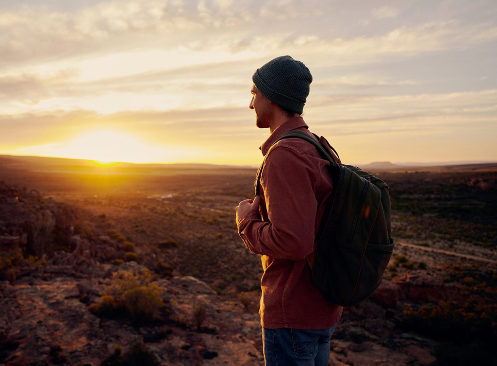 Hiker with backpack overlooks terrain at sunrise