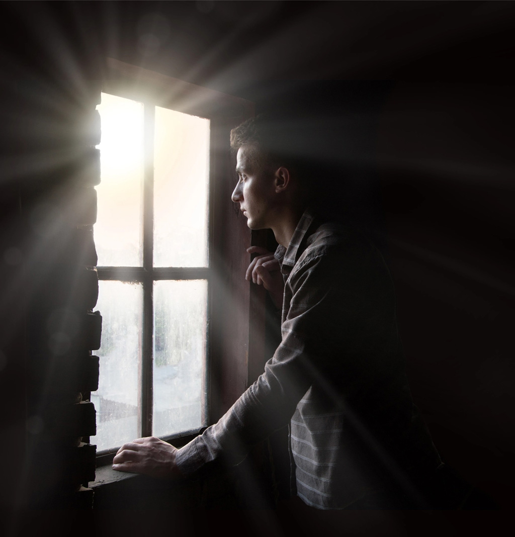 Young man looking out bright window hopeful